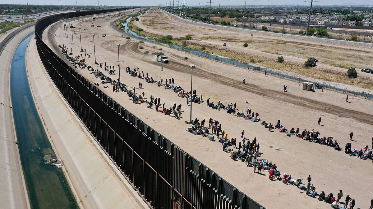 Migrants wait along border wall