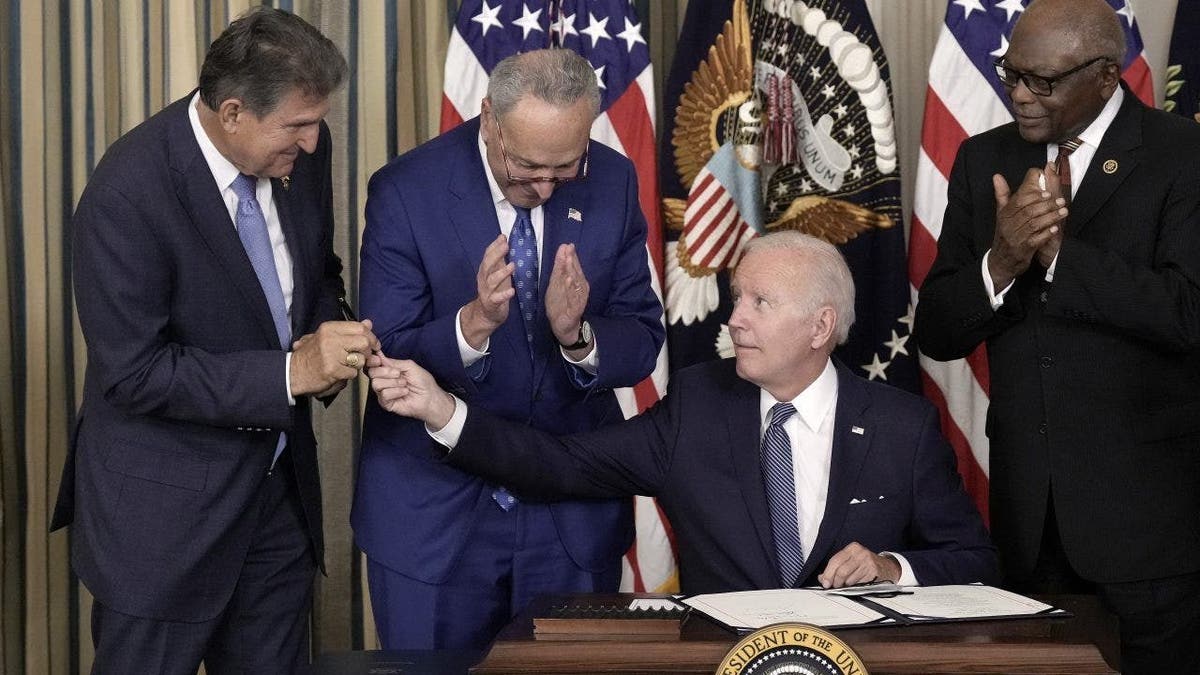 President Joe Biden (C) gives Sen. Joe Manchin (D-WV) (L) the pen