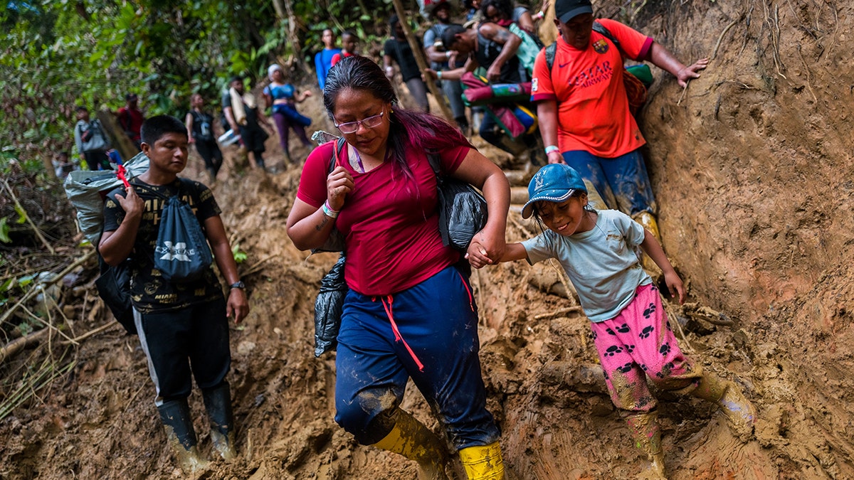 Ecuadorian migrants climb down a muddy hillside trail in Darién Gap, Colombia