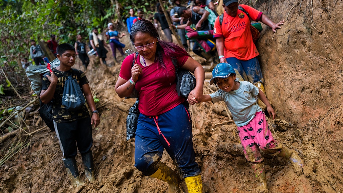 Ecuadorian migrants climb down a muddy hillside trail in Darién Gap, Colombia