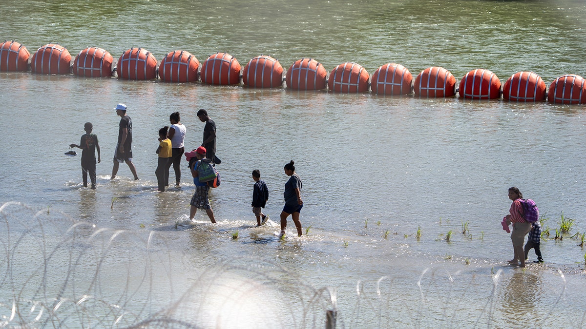 Migrants walk near the floating barrier in the Rio Grande