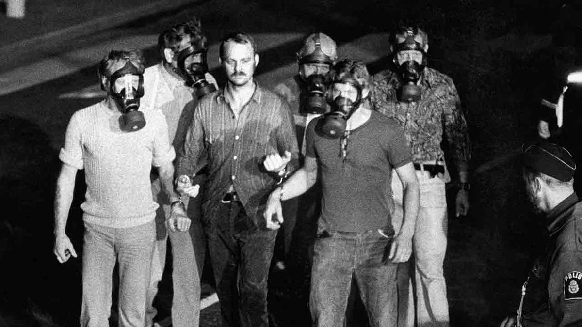 Man being led away by police officers who are wearing gas masks