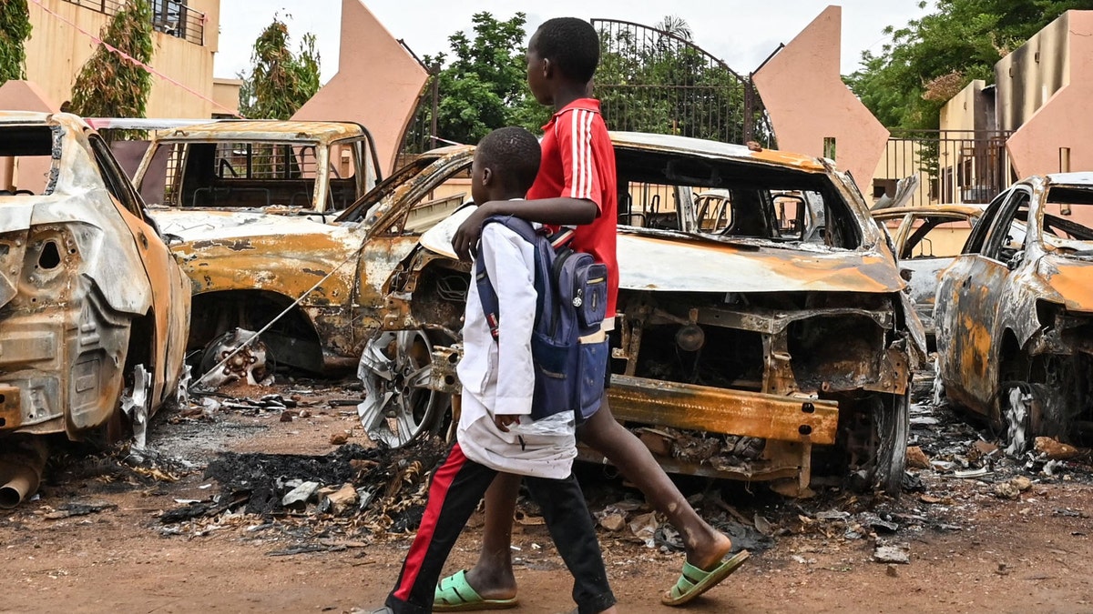 burned out cars on street as children walk by