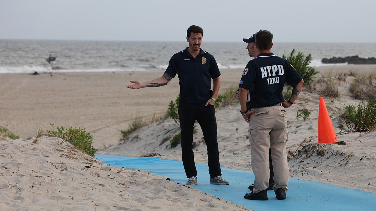 NYPD officers stand on Rockaway Beach after shark attack