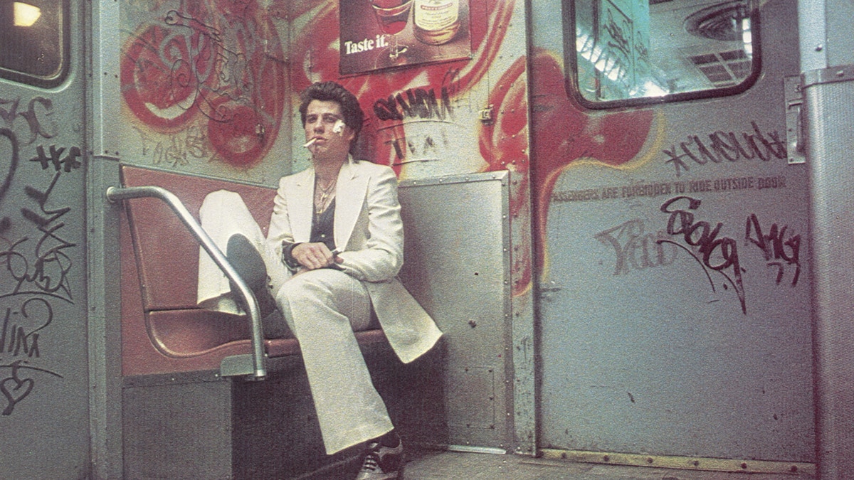 John Travolta sitting in a white suit in a scene from "Saturday Night Fever"