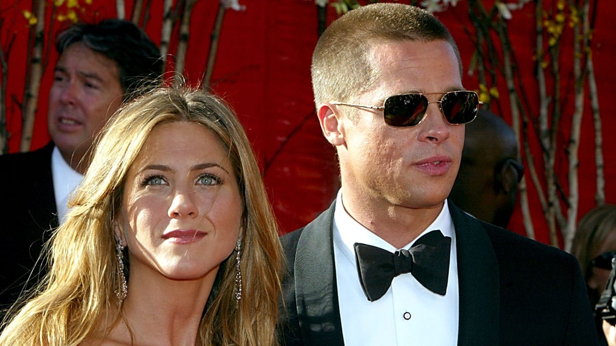 Jennifer Aniston looks off in the distance at the Emmy Awards carpet while Brad Pitt wheres a tuxedo and sunglasses