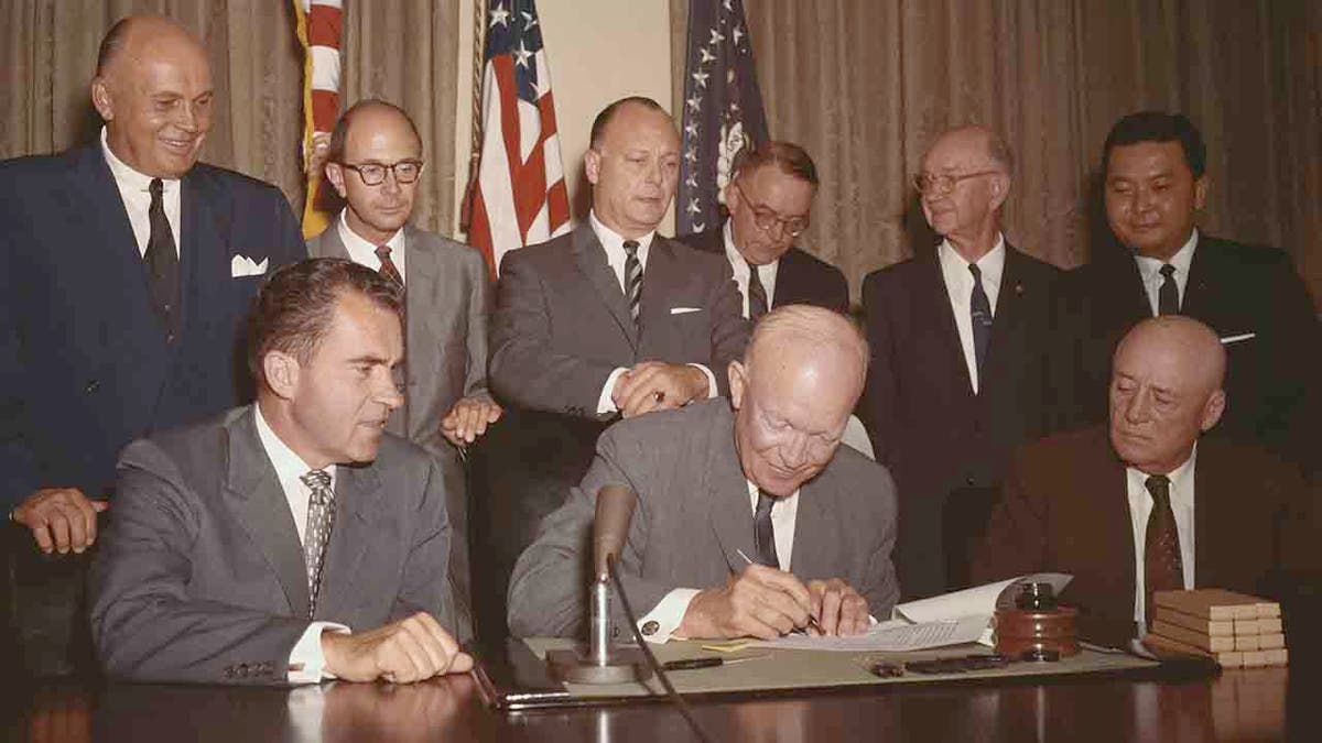 Dwight Eisenhower signing paper as Richard Nixon, and others look on