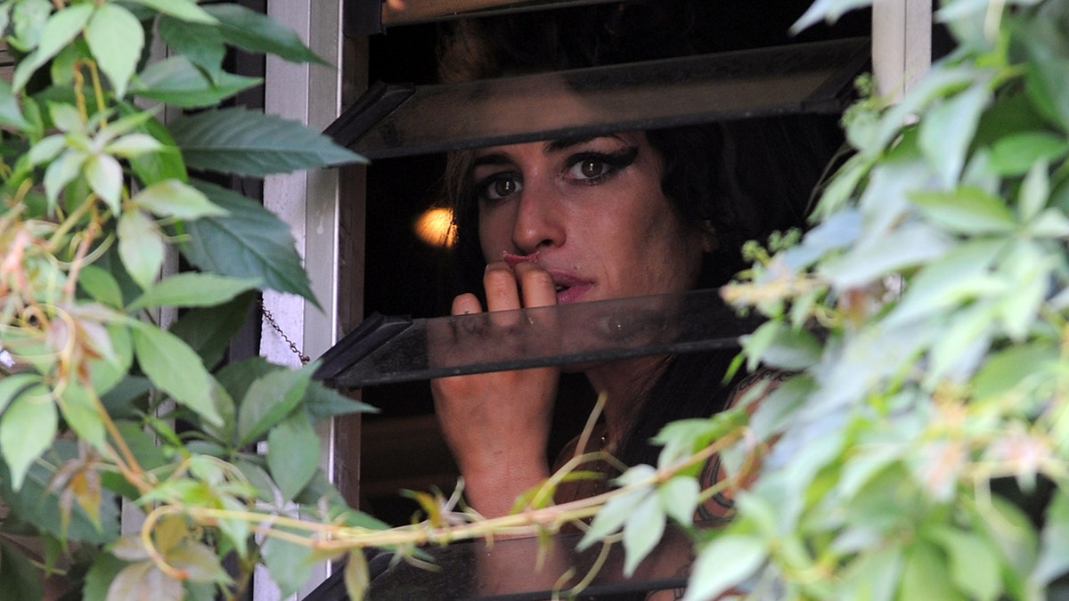 Amy Winehouse looking fron a window surrounded by vines