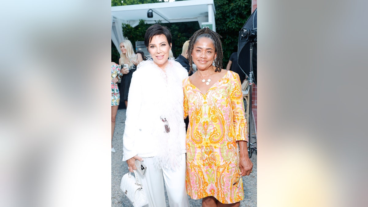 Kris Jenner wearing a white suit and Doria Ragland wearing an orange and pink dress