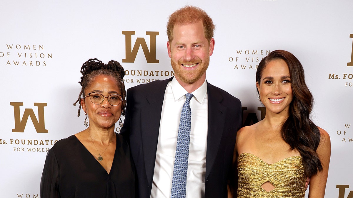 Doria Ragland wearing a black dress, Prince Harry wearing a suit and light blue tie and Meghan Markle wearing a gold dress