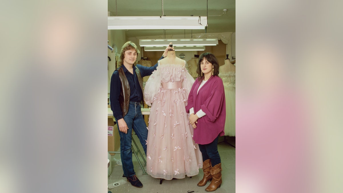 David Emanuel and Elizabeth Emanuel standing in between a pink dress