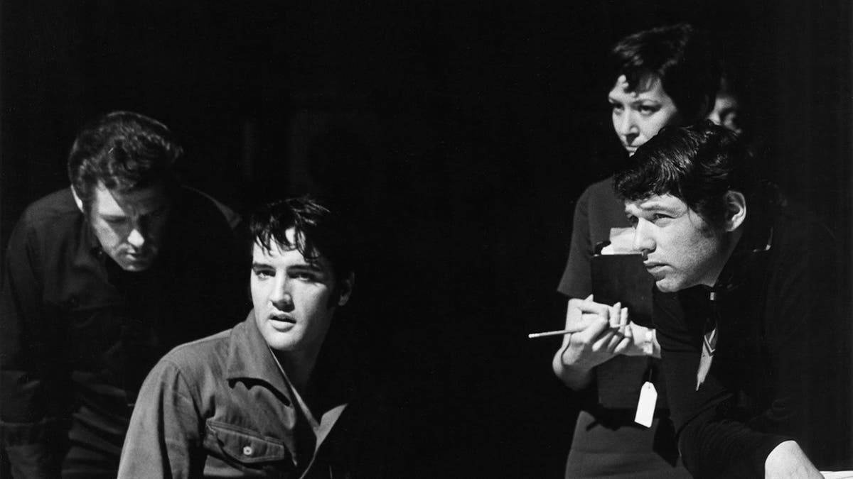 Elvis Presley looking away as he suits next to several men on stage