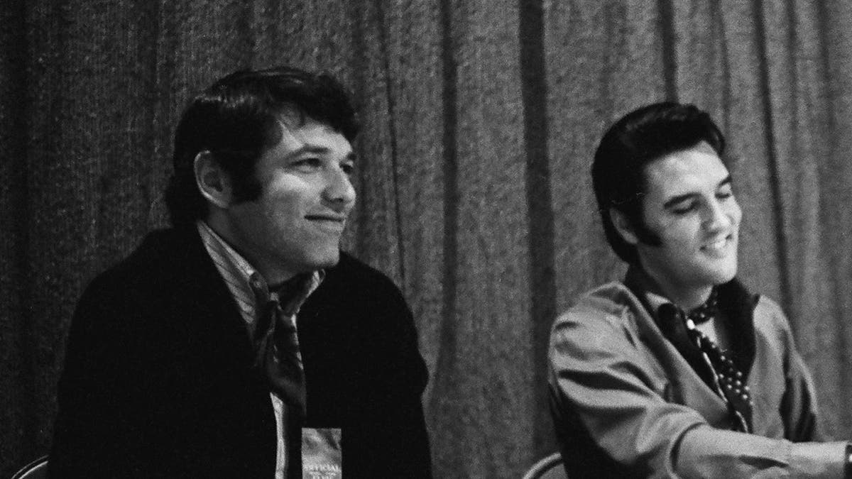 A close-up of Steve Binder and Elvis Presley sitting together and smiling