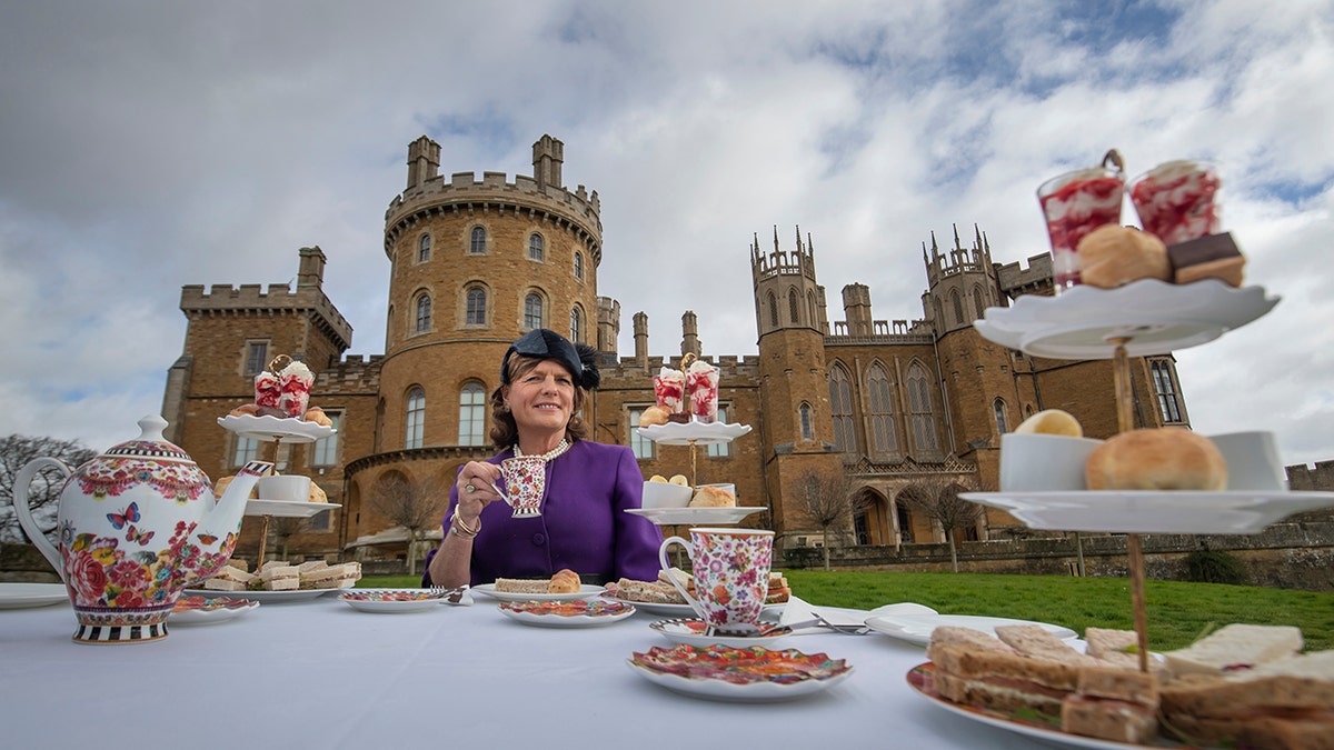 Emma Manners wearing a purple dress with a matching hat having tea outside Belvoir Castle