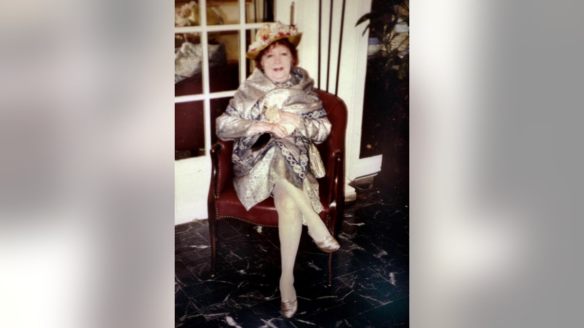 Irene Silverman wearing a silver coat while sitting on a ruby red couch