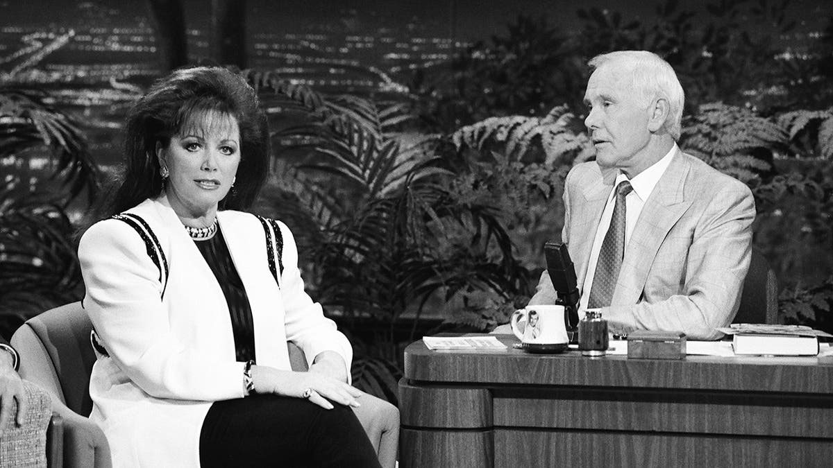 A black and white photo of Jackie Collins being interviewed by Johnny Carson