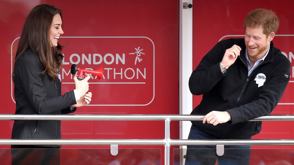 Kate Middleton laughing and blowing a horn in front of a startled Prince Harry