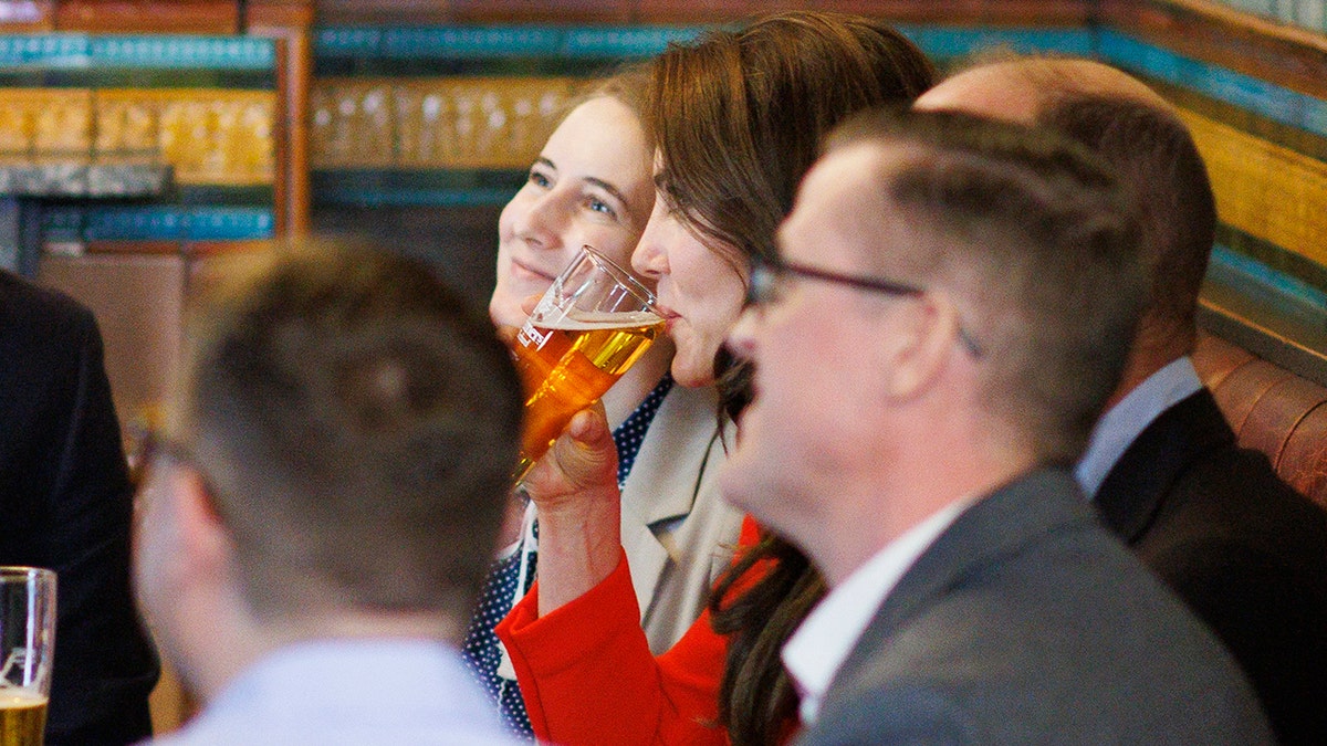 Kate Middleton wearing a red dress drinking a beer