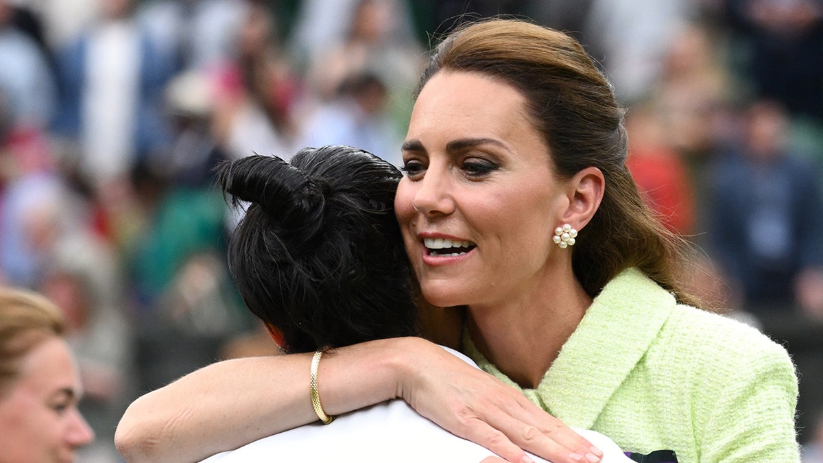 Kate Middleton in a lime green dress hugging a woman on the field