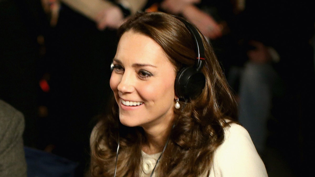 A close-up of Kate Middleton wearing a white sweater and headphones