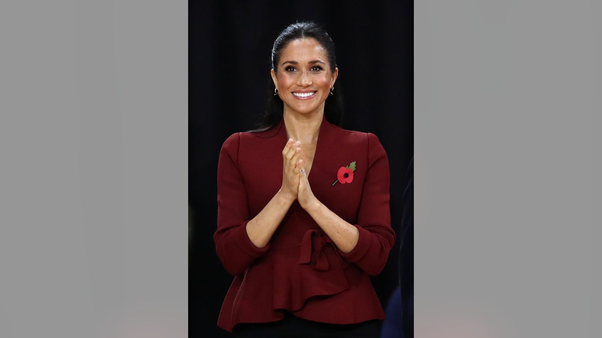 Meghan Markle wearing a burgundy sweater with a red flower pin