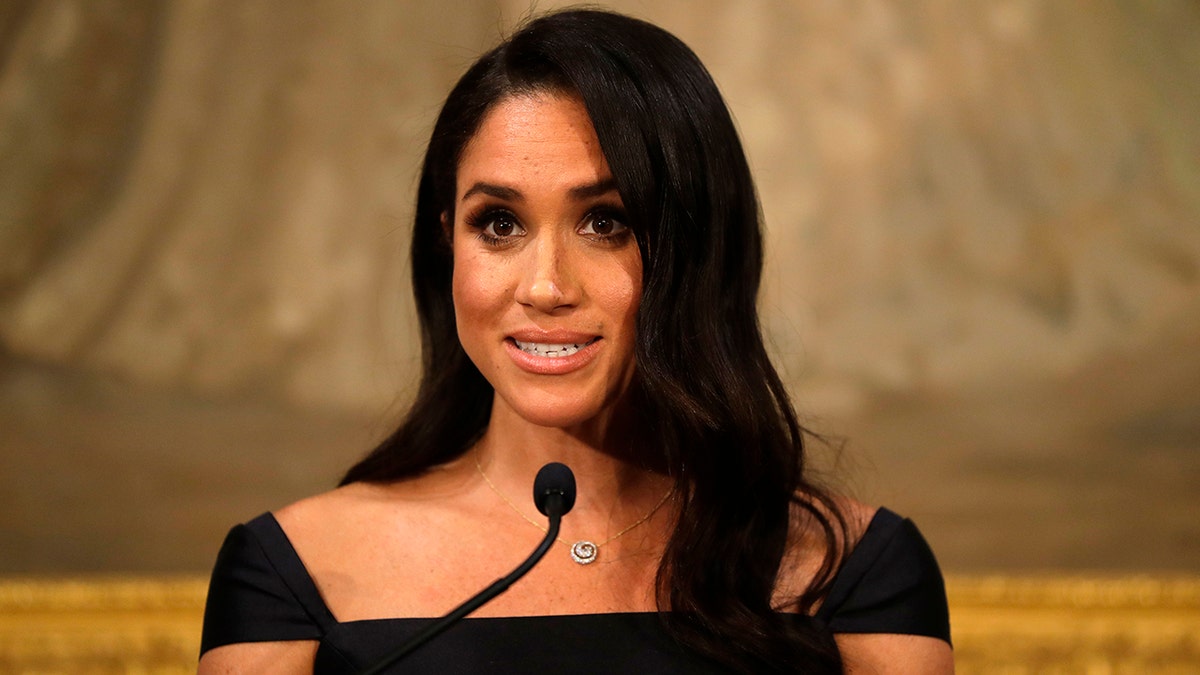 A close-up of Meghan Markle wearing a black dress speaking to the podium