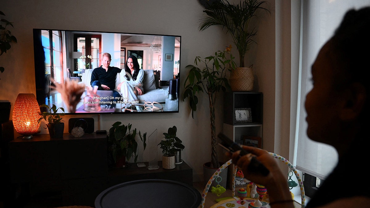 A woman in the background watching Prince Harry and Meghan Markle's Netflix documentary