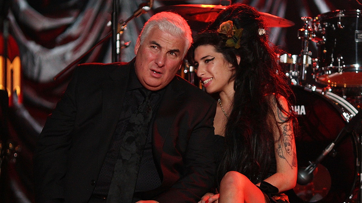 Amy Winehouse leaning next to her father as they both wear black on stage