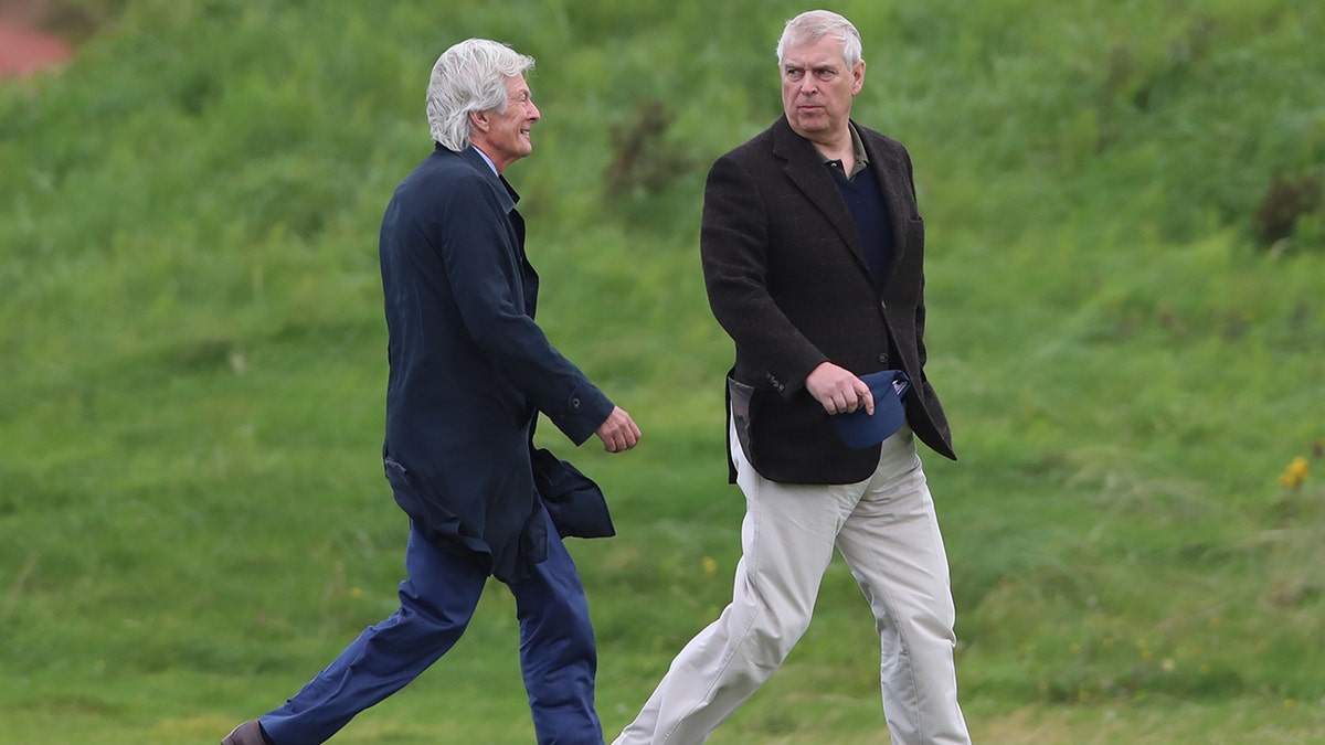 Prince Andrew in a black blazer and white slacks talking to Paul Tweed in a navy coat and blue jeans in a field