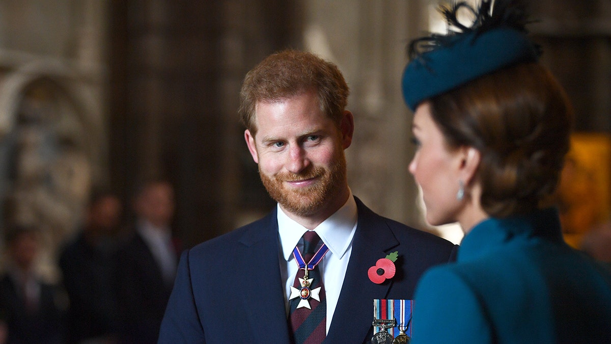 Prince Harry in a suit and tie admiring Kate Middleton in a blue dress with a matching fascinator