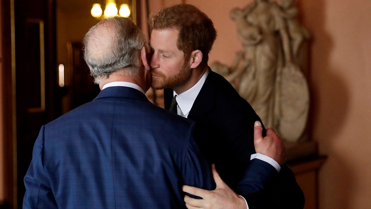 King Charles with his back turned being kissed on the cheek by Prince Harry
