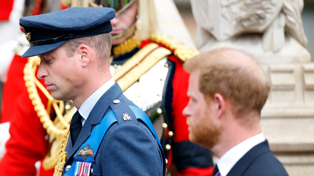 Prince William in a military suit marching in front of Prince Harry wearing a suit