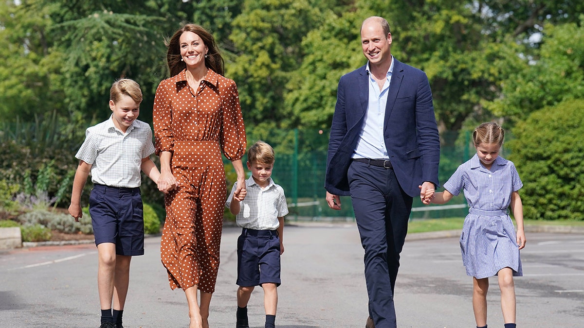 Kate Middleton in a polka dot brown dress walking alongside Prince William and their three children as they wear various shades of blue and white