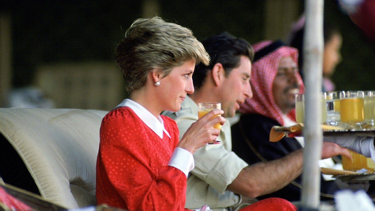 Princess Diana wearing a red and white dress drinking next to Prince Charles