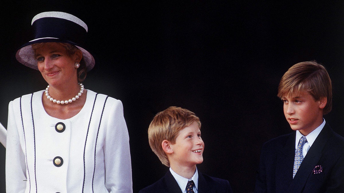 Princess Diana in a white and navy dress with a matching hat standing next to Prince Harry and Prince William