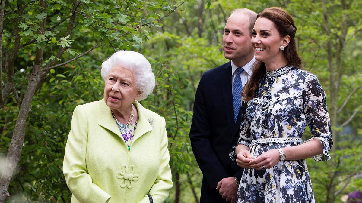 Queen Elizabeth wearing a neon green dress next to Kate Middleton in a multicolored dress and Prince William in a navy suit and tie