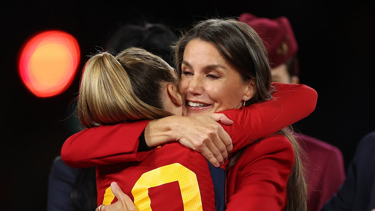 Queen Letizia hugging a football player wearing a red blazer