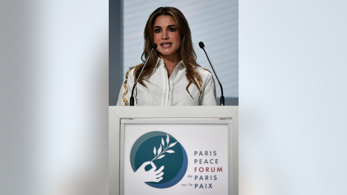 Queen Rania of Jordan wearing a white blouse speaking in front of a podium