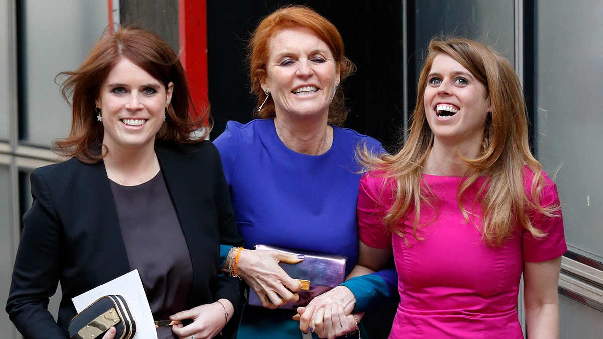 Sarah Ferguson wearing a blue dress in the arms of her two daughters as they all laugh