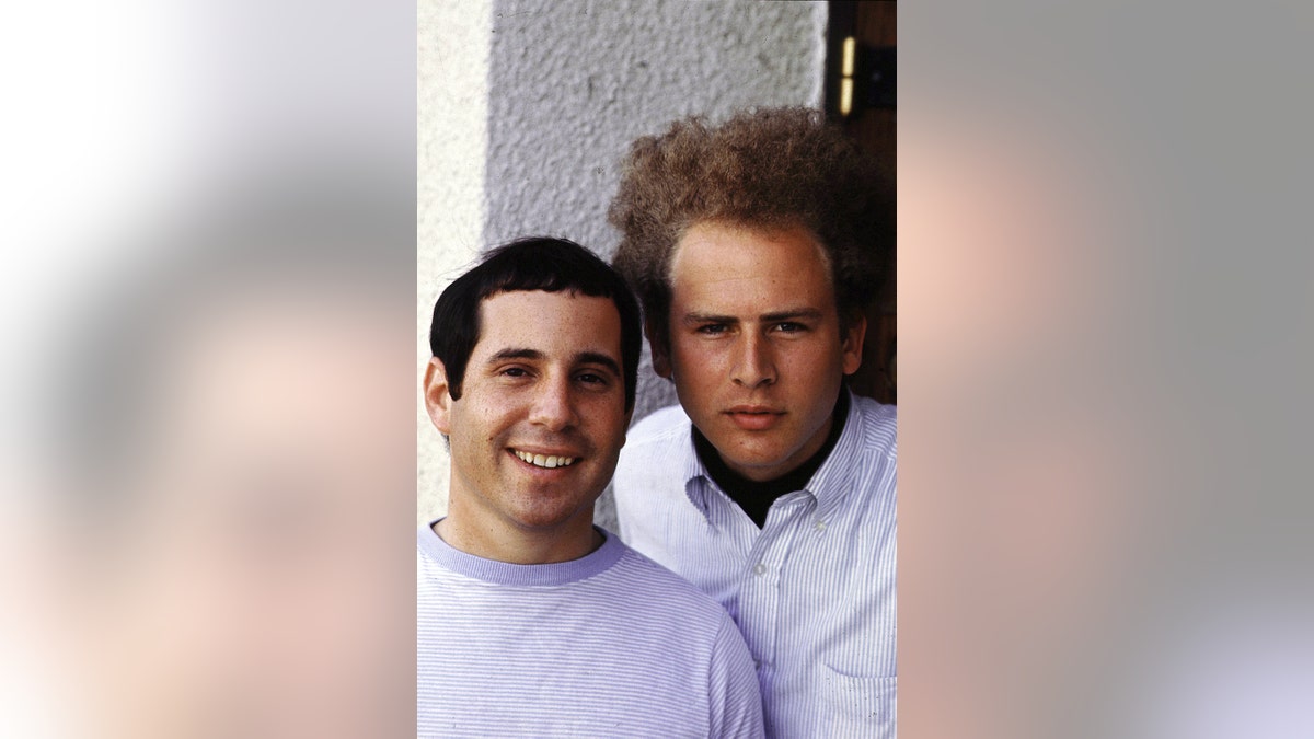 Paul Simon and Art Garfunkel leaning close to each other for a photo