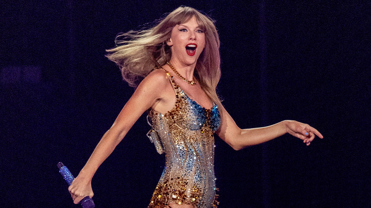 A close-up of Taylor Swift wearing a sparkling costume on stage while she holds a mic