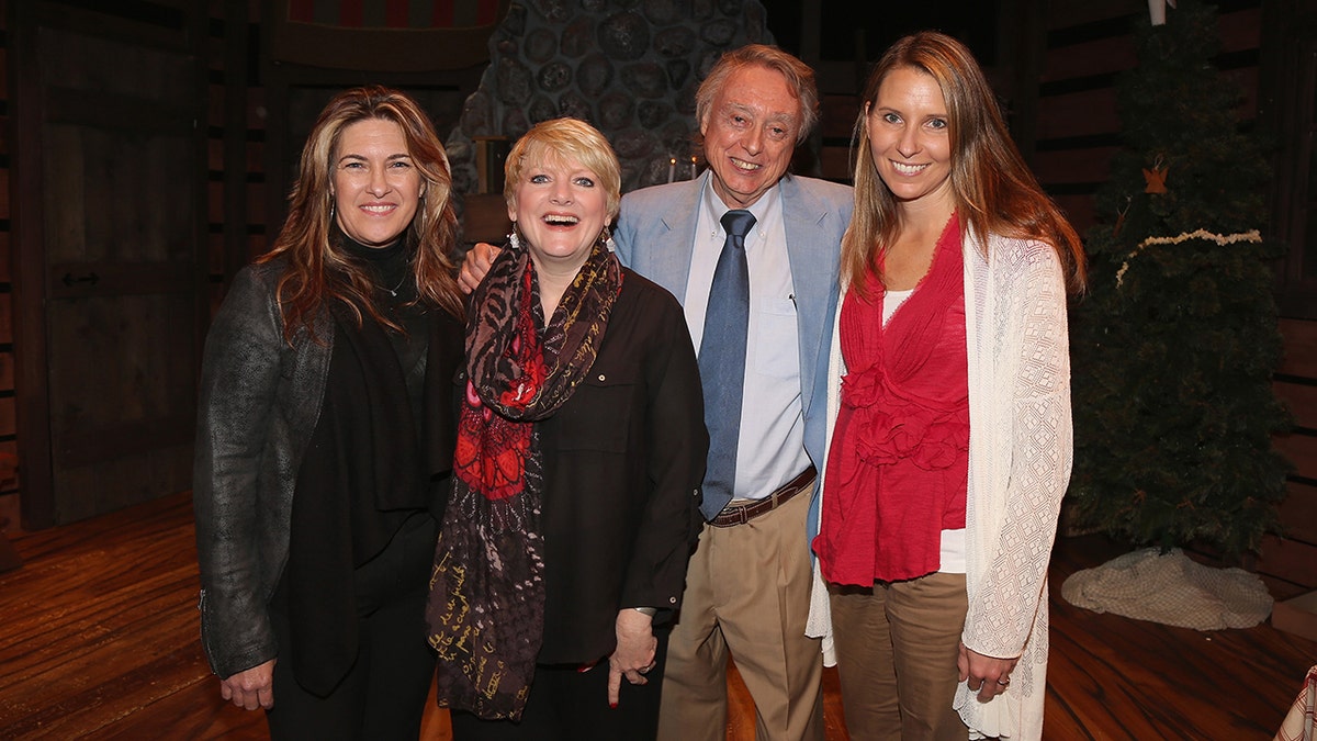 Wendi Lou Lee wearing a red vest and a white sweater posing with castmates of Little House
