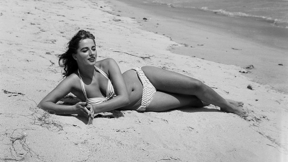 A glamour shot of Jackie Collins posing in a bikini at the beach