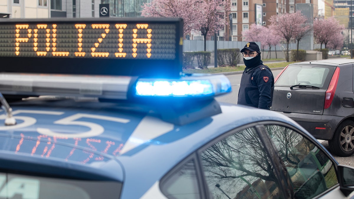 Italian police officer stands outside a police car