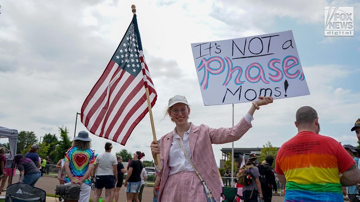 The protester holds a sign saying: "This is NOT a phase, moms!"