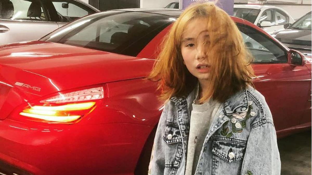 Lil tay poses by red sports car wearing denim coat