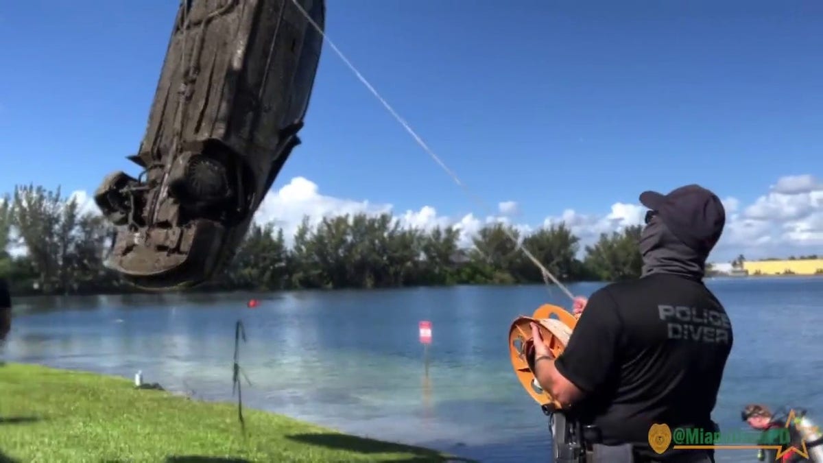 police officer looks on as submerged car removed from lake