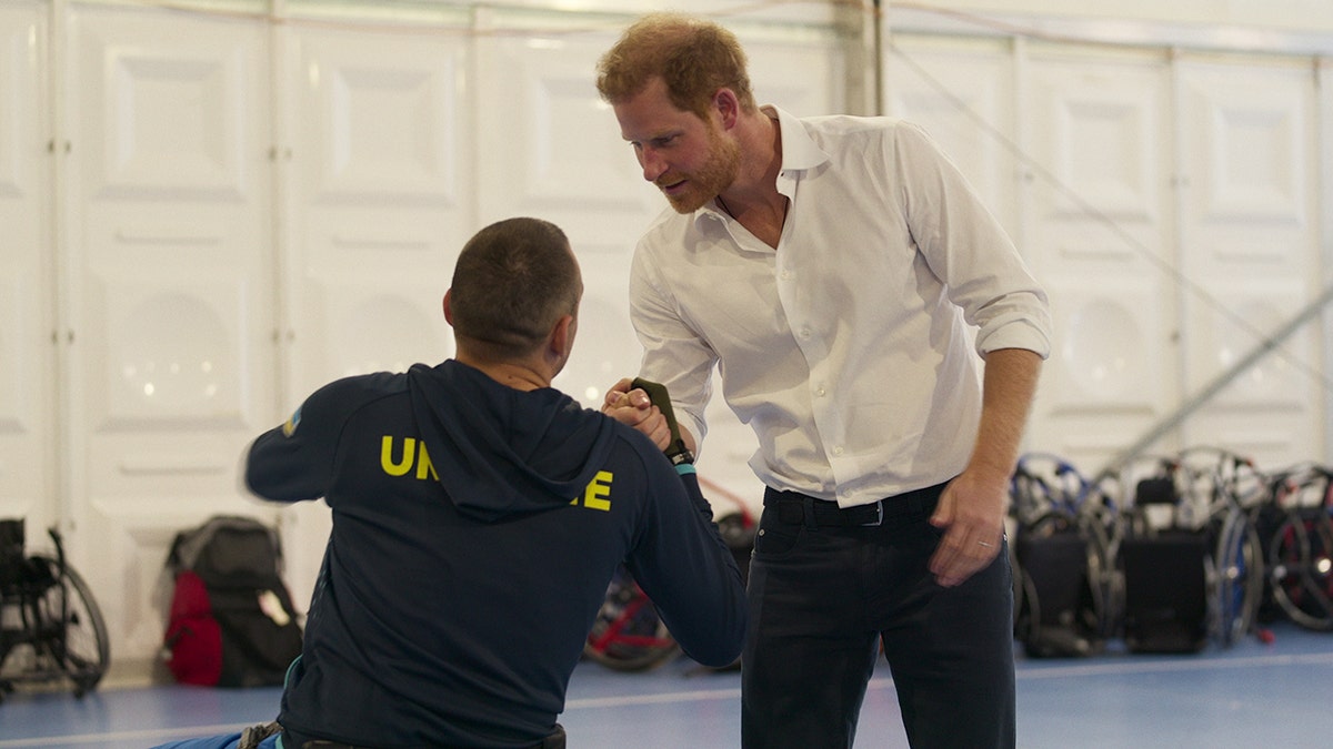 Prince Harry in a white shirt and dark pants greeting a sports competitor