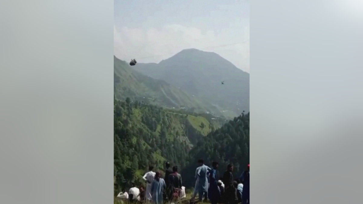 Crowd watches gondola that is stuck in the air in Pakistan