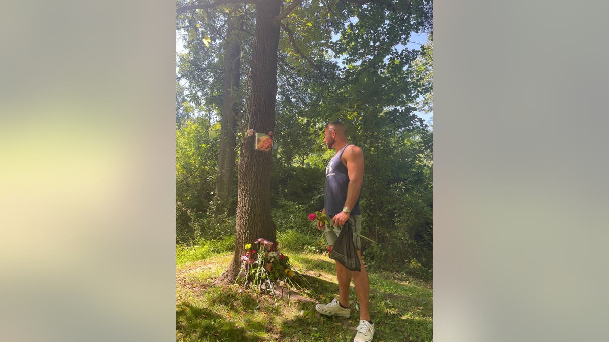 Richard Tobin stares at a tree trunk with a picture of Rachel Morin taped to it.